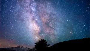 Milky Way galaxy spanning over a peaceful silhouetted mountain landscape at night.