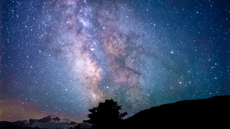 Milky Way galaxy spanning over a peaceful silhouetted mountain landscape at night.