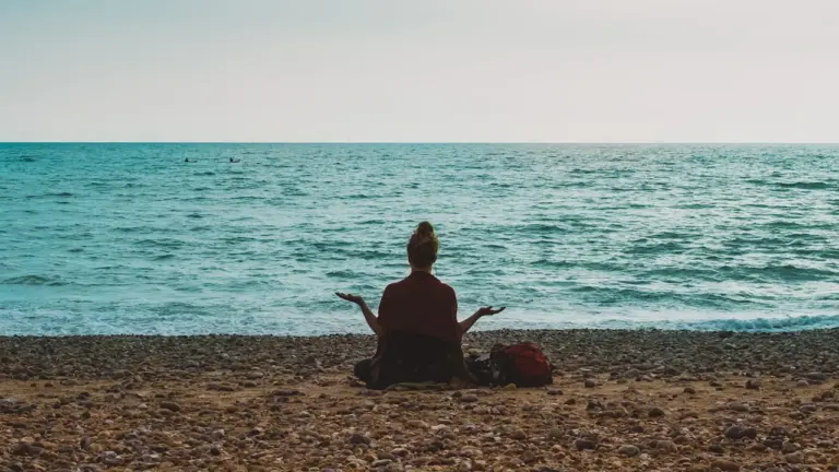 Person practicing yoga and meditation on the pebbled shore of Brighton Beach, England.