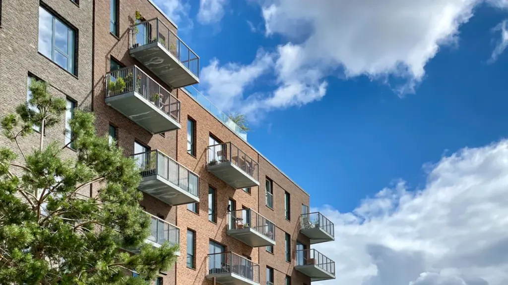 Modern residential apartment building with brick facade under a bright blue sky.