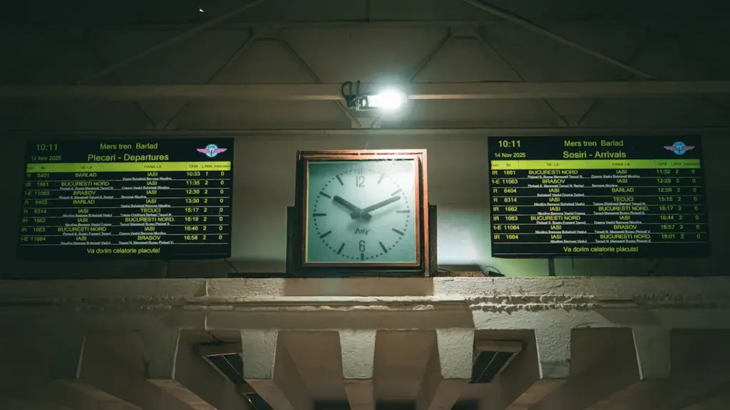 An analog clock centered between two train station departure and arrival boards.