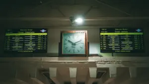 An analog clock centered between two train station departure and arrival boards.