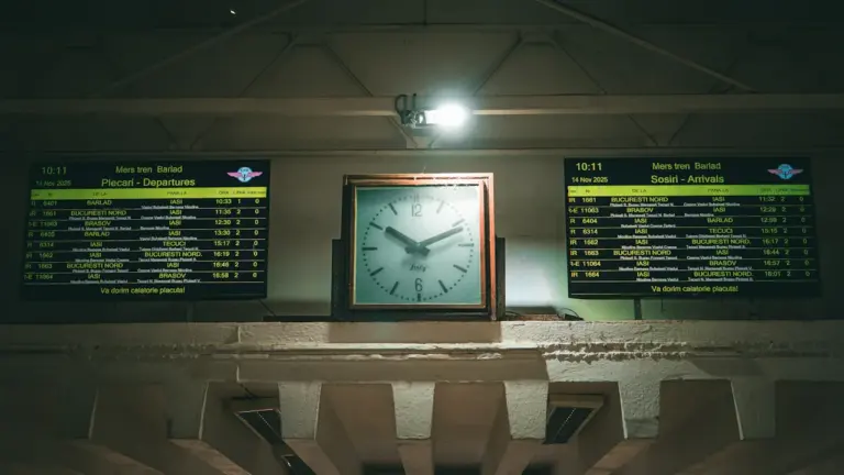 An analog clock centered between two train station departure and arrival boards.