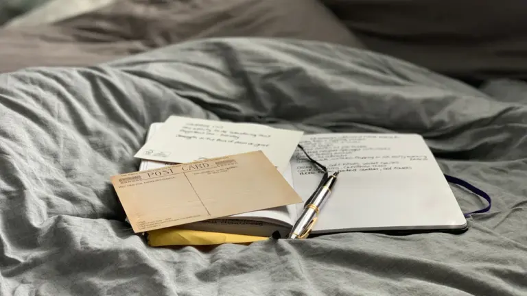 An open journal with a fountain pen resting on a grey duvet.