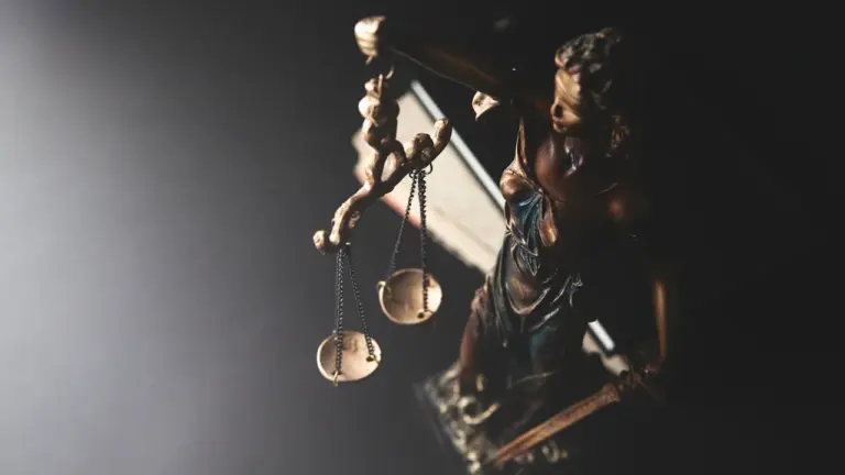 Statue of Lady Justice holding golden scales against a dark moody background.